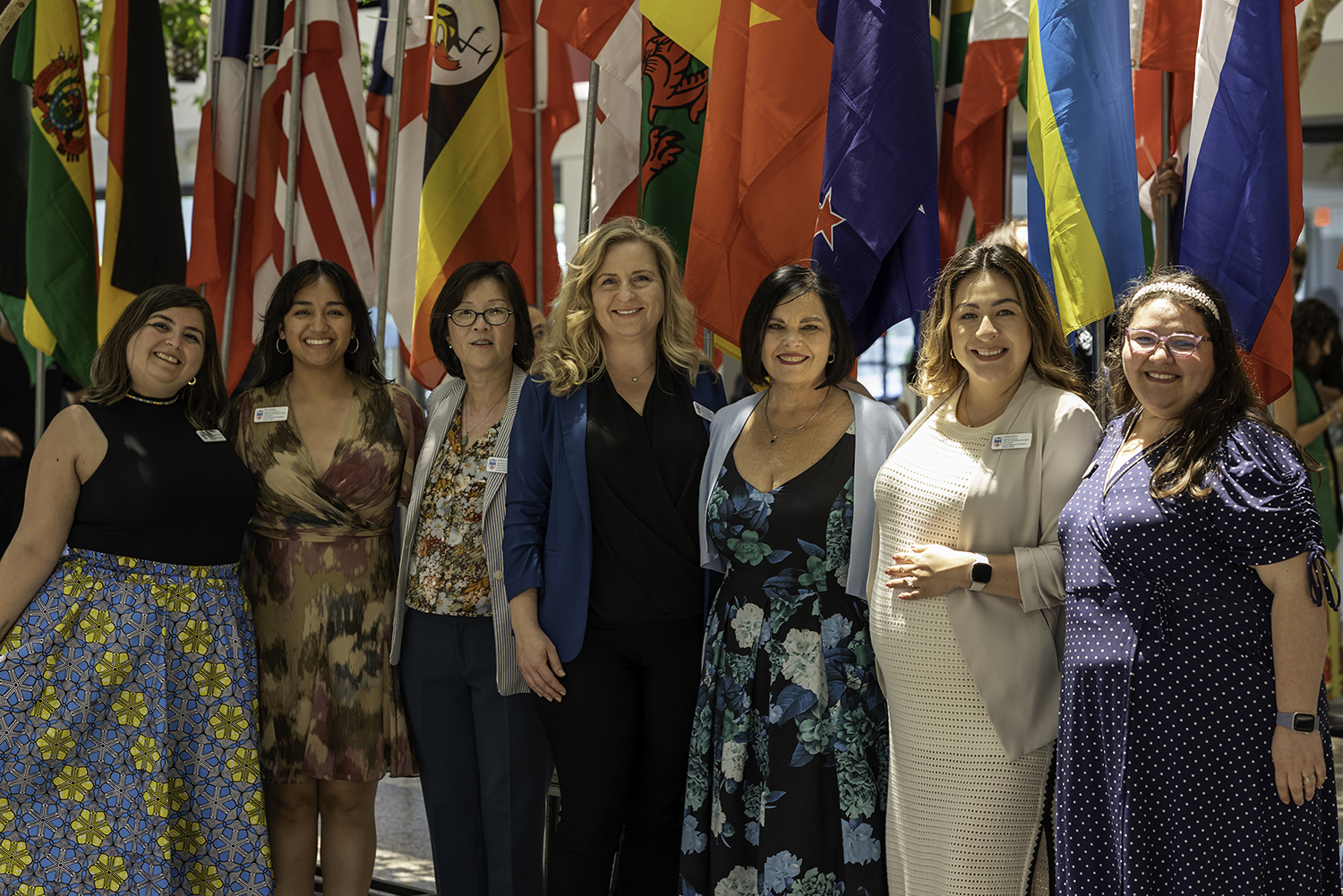 A group picture of the members of the Office for International Students and Scholars, 3/4 body, in front of international flags.